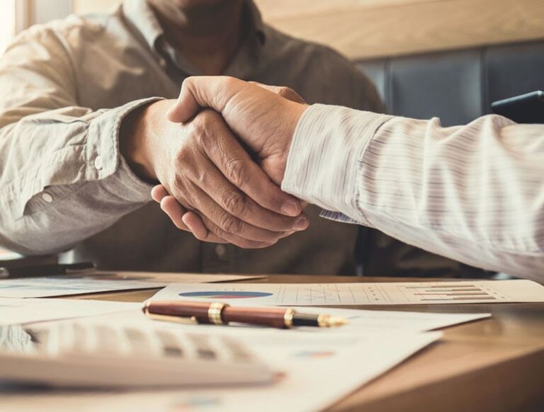 A business energy broker and a business owner shaking hands over a signed deal for a cheaper energy rate.