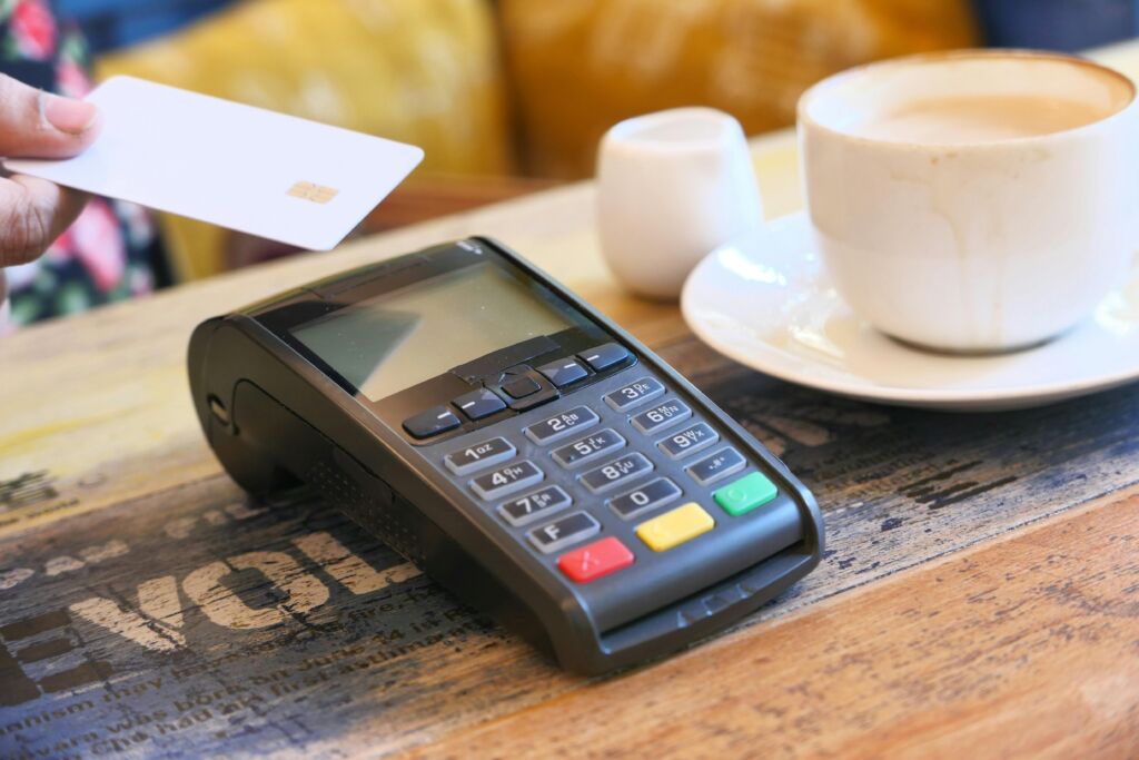 A business card machine on a table with a credit card ready for swiping, alongside a cup of tea.